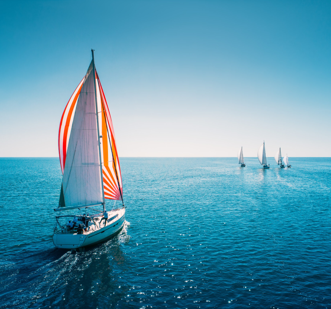 Regatta sailing ship yachts with white sails at opened sea. Aerial view of sailboat in windy condition.